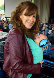 Baby with headphones and matching Moby wrap enjoying live music concert with his mom.
